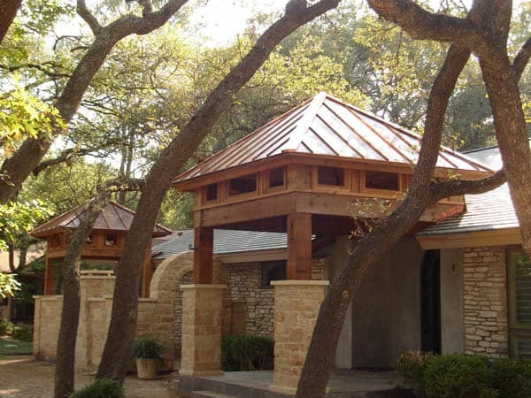 Standing-seam copper pavilion roof over a wood-beamed porch, oak trees framing the view