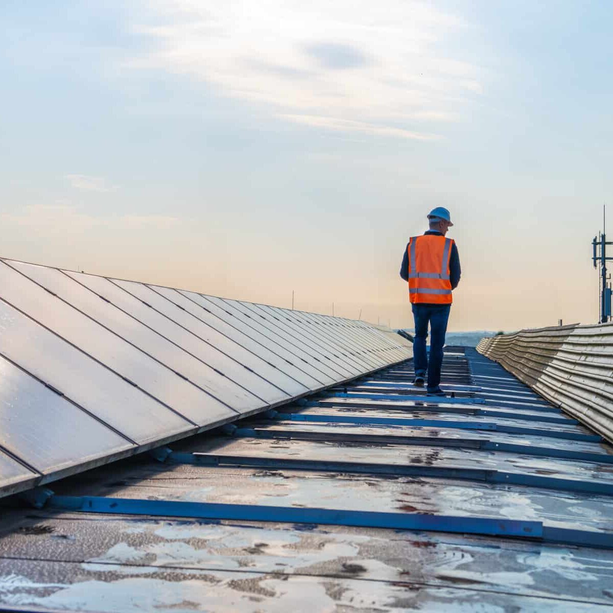 Rear view of mature male engineer walking along the rows of photovoltaic panels on a rooftop of a solar plant.